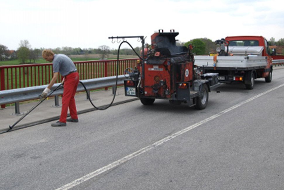 Ein Mitarbeiter mit einem Auto und einem Anhänger mit der Maschine auf einer Straße