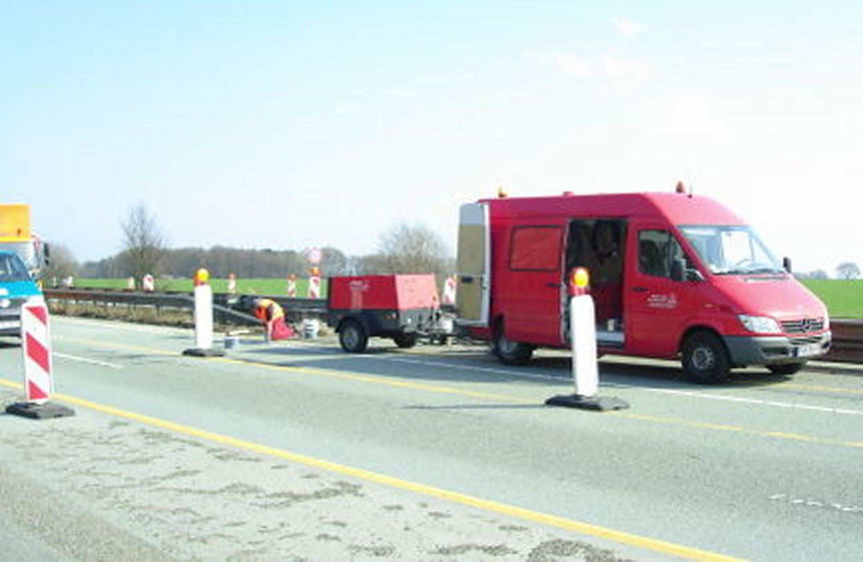 A red Sprinter with a machine on a road with road damage