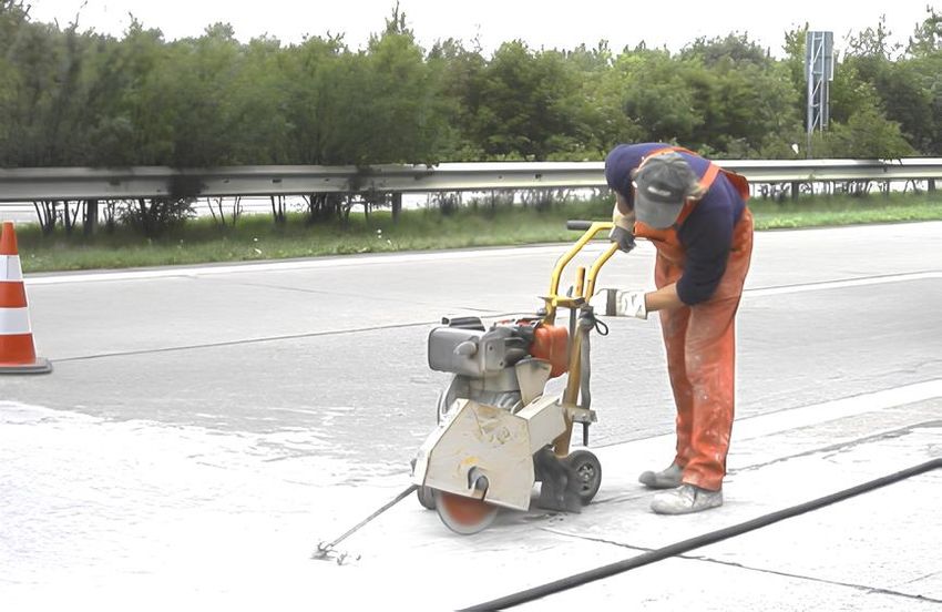 A man in work clothes cuts asphalt with a machine